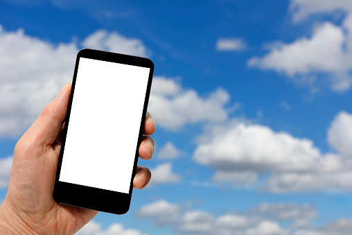 Close-up of hand holding a smartphone with blank screen against blue sky.