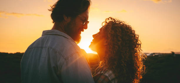 Man and woman adult relationship in outdoor love leisure activity enjoying golden sunset and looking each other with love and tenderness. People attraction lifestyle. Emotions and feeling on vacation stock photo
