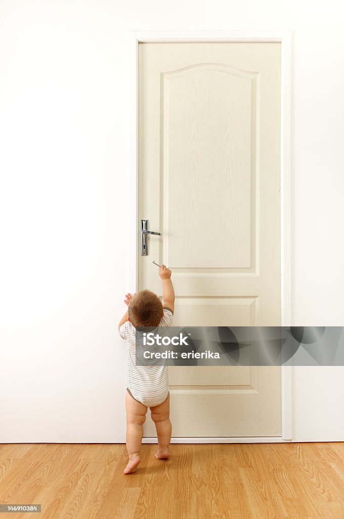 Cute toddler reaching for door's handle ready to go Baby in front of a closed door, trying to reach the keyhole with key Child Stock Photo