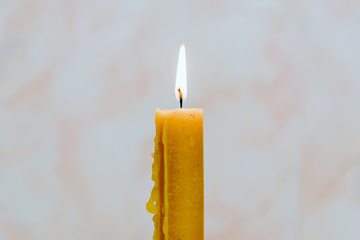 Candle light for spirituality ceremony against grey blurred background.Hot wax drips from the candle.Copy space.