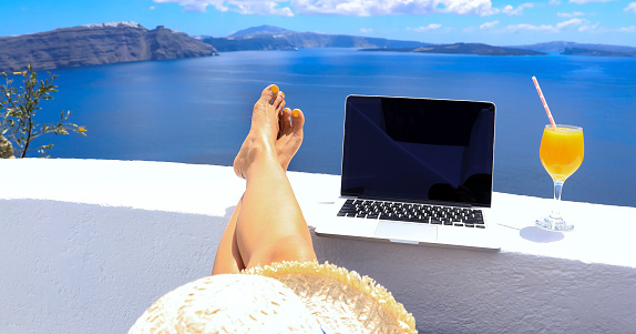 Digital nomad freelancer woman  lying and sunbathing as  remotely with bright scenic view of the Mediterranean Sea ,Oia -Santorini,Greece