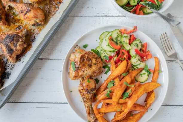 Delicious, healthy and gluten free dinner or lunch with baked chicken, sweet potato fries and zucchini, bell pepper salad. Served ready to eat on a plate on white table background. Flat lay