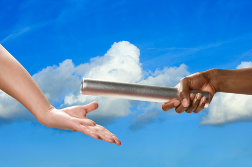 Baton handoff with white clouds and blue sky in background. Horizontal format.