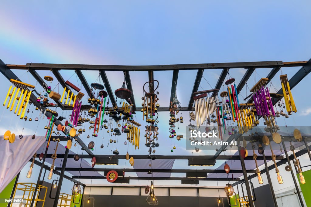 Wind chimes of deferent pattern hanging high up on a wooden structure Wind chimes of deferent pattern, material and designs hanging high up on a wooden structure with rainbow background Abstract Stock Photo