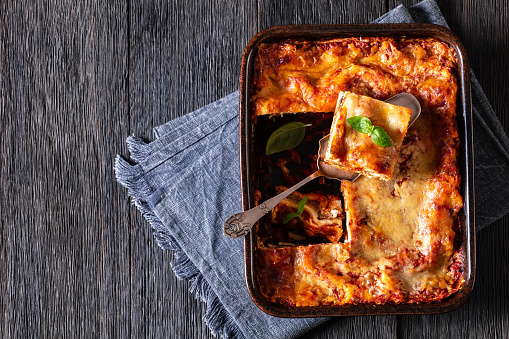 Lasagna with ricotta cheese, ground beef, mushrooms, and tomato sauce in baking dish on dark wooden table, horizontal view from above, flat lay, copy space