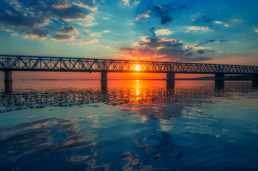 Majestic sunrise over bridge across the Dnieper river near Cherkasy, Ukraine. Beautiful clouds and colorful water in river reflected at the autumn morning
