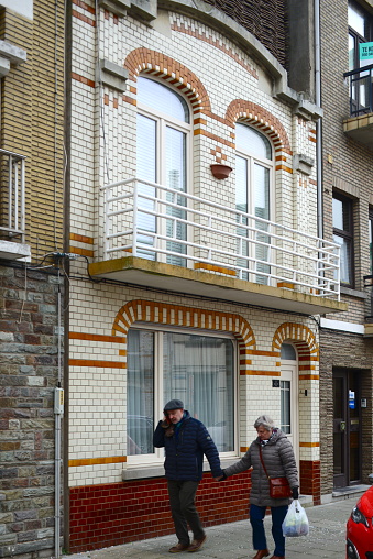 Blankenberge, West-Flanders, Belgium- February 22, 2023: senior couple holding hands in front of typical heritage Art Deco building with yellow shiny facade tiles on Belgian coast