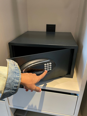 Stock photo showing close-up view of a hotel closet safety deposit box with open door, for valuables and money with electronic display and keypad being used by an unrecognisable person.