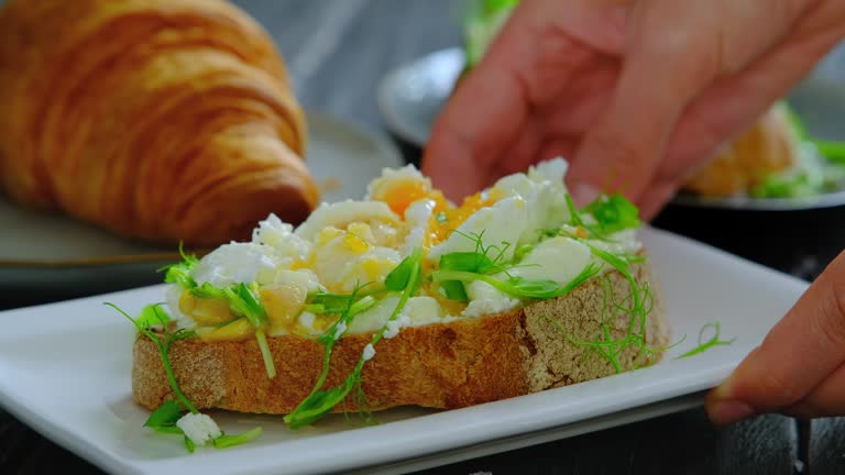 Woman's hands putting a plate with poached egg on avocado toast on table. Benedict egg with avocado spread, close-up video, 4k video