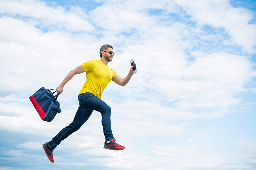 Energetic man running with travel bag midair sky background, copy space.
