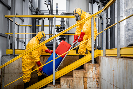 Workers in yellow protection suits and respiratory full face masks carrying aggressive substances or hazardous materials for chemical industry. Production of acids for industry.