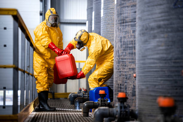 istock Chemical worker carrying canisters with hazardous materials and standing by large storage acid tanks. 1469128380