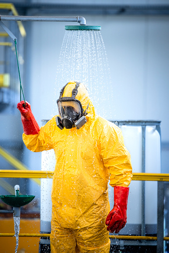 Chemical worker taking a shower and washing off aggressive chemicals after accident in acid production factory. Safety at work and workers health care.