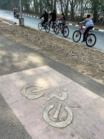 Chandigarh, India - January 1, 2023: Stock photo showing close-up, elevated view of cycle lane symbol painted on empty, tarmac pathway with cyclists riding bicycles on road in residential district. Chandigarh is the capital city of both the states of Punjab and Haryana.