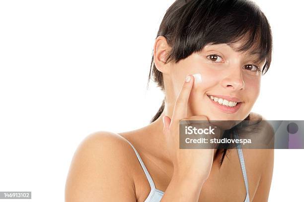 A Young Brunette Girl Applying A Cream To Her Cheek Stock Photo - Download Image Now