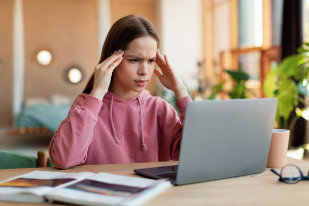 istock Exhausted schoolgirl suffering from headache, overworking, having too much online homework, looking at laptop 1469136912
