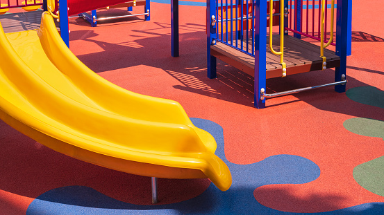 Slider with playground climbing equipment on colorful rubber floor in outdoors playground area