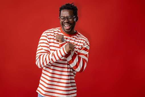 Cheerful black man having fun while dancing against red background. Copy space.
