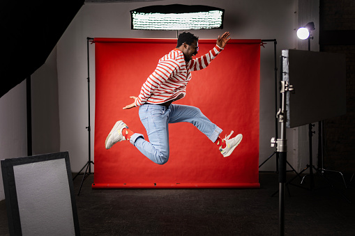 Side view of cheerful African American man having fun while jumping in a photo studio. Copy space.