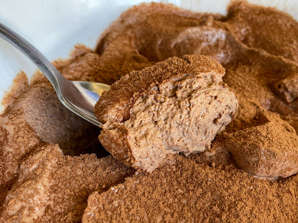 A bowl of chocolate mousse being eaten with a spoon, with cocoa powder dusted on top of the delicious, indulgent dessert, served in white crockery. stock photo