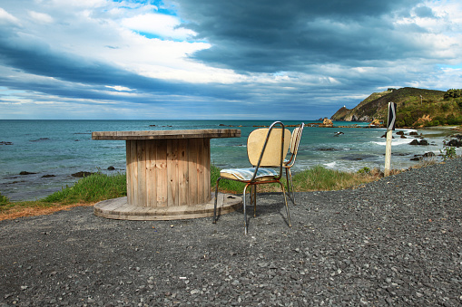 The beach at Kaka Point in New Zealand with street furniture during rough weather with a moody and cloudy sky.