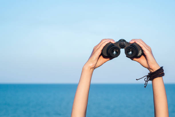 istock Female hands hold binoculars on the blue horizon, sky and sea background 1469145688