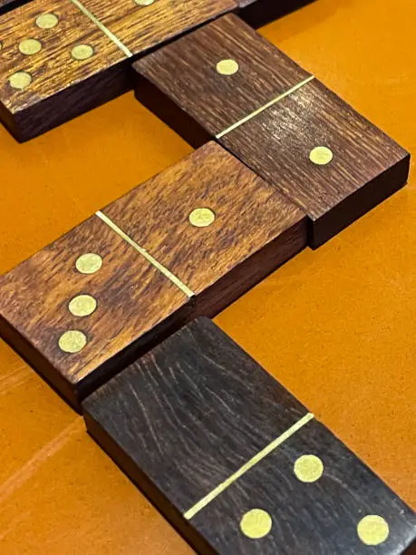 Photo of Image of wooden domino game on orange coloured table, matching numbers and zig zag path in famous, popular board game, elevated view