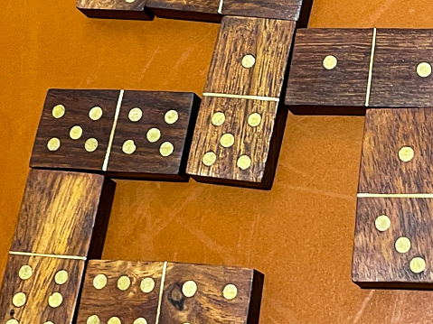 Stock photo showing a game of wooden dominoes being played on top of an orange table. This is a popular tabletop board game that is known internationally, and is the national game of Cuba, in which players must match numbers in branching paths