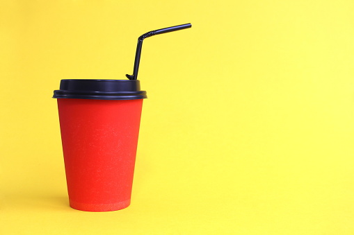 On a yellow background, there is a red glass with a lid and a straw for takeaway hot drinks.