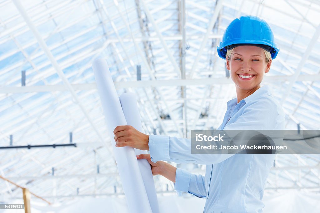 Felice giovane architetto femmina holding cianografie in Cantiere di costruzione - Foto stock royalty-free di 20-24 anni