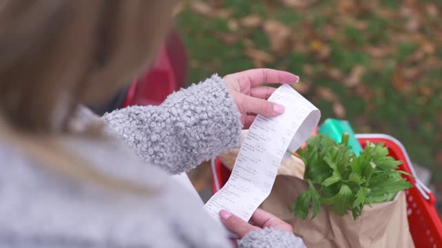 The buyer checks the paper receipt after shopping in the supermarket. Customer check account, expensive total. Cash Register Money Spending On Hypermarket. Home Finance Budget.Woman Check Bill Grocery Store Shopping Cart