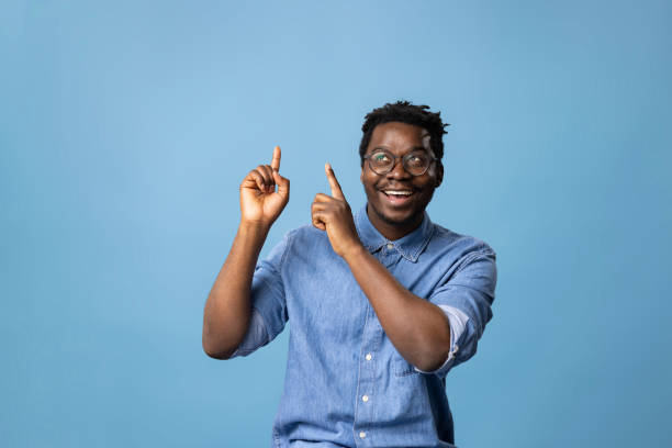 Look up here! Portrait of happy African American man showing empty space on blue background. Copy space. point stock pictures, royalty-free photos & images