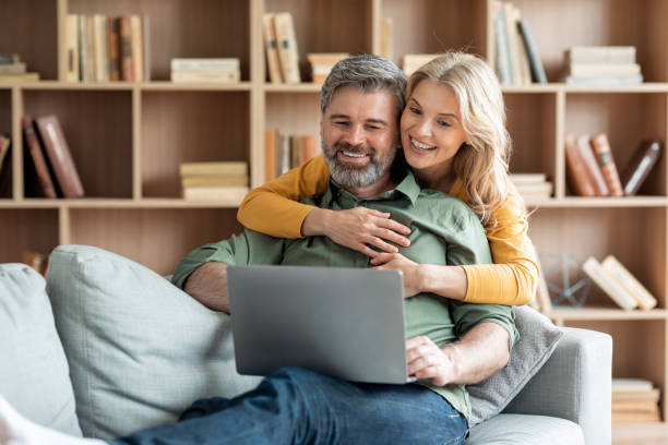 istock Smiling Middle Aged Spouses Spending Time With Laptop In Living Room 1469154351