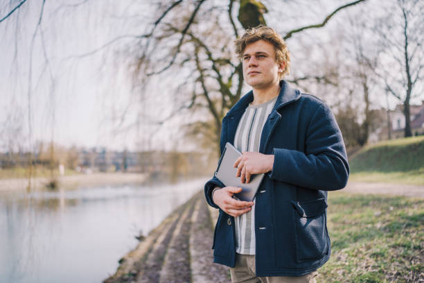 istock Front view of young man using digital tablet outside in the park next to river. Copy space. stock photo 1469158649