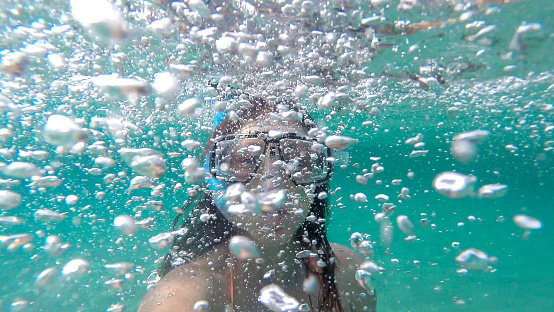 A girl is snorkeling, fully submerged in water and surrounded by airbubbles. The sea or ocean water is in beatyfull blue color.