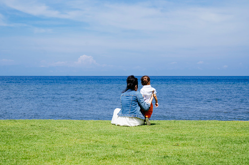 asian woman  sitting on the grass and  playing with her   baby on the beach