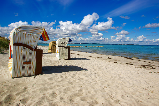 Sand coast line with a blue, slightly cloudy summer sky and beach furniture located at the baltic sea, typical european beach vacation and travel scene.