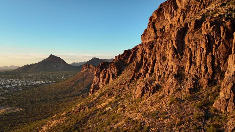 Cinematic aerial shot passing rocky peaks of desert mountains revealing Tucson Arizona, slowing rising and rotating POV drone