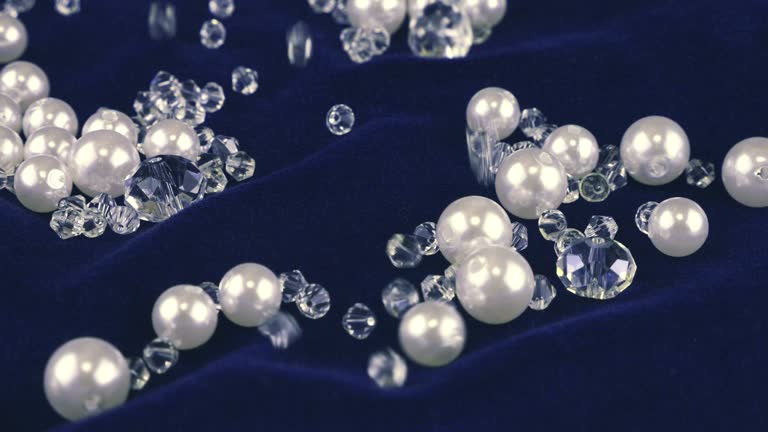 Transparent white jewelry crystals, rock crystal and pearls fall on dark blue velvet.