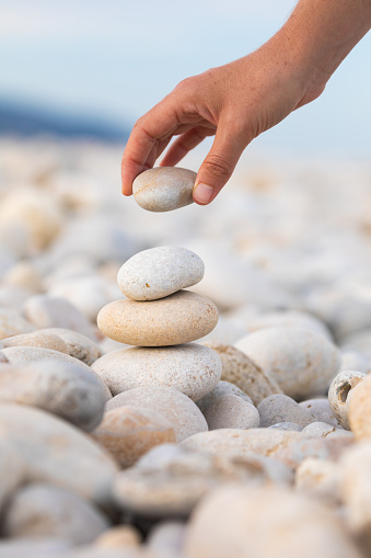 A young woman's hand stacks several rounded stones on a beach in search of balance and harmony