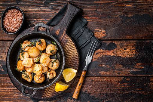 Scallops seared in garlic, thyme and butter served in cast iron skillet. Wooden background. Top view. Copy space.