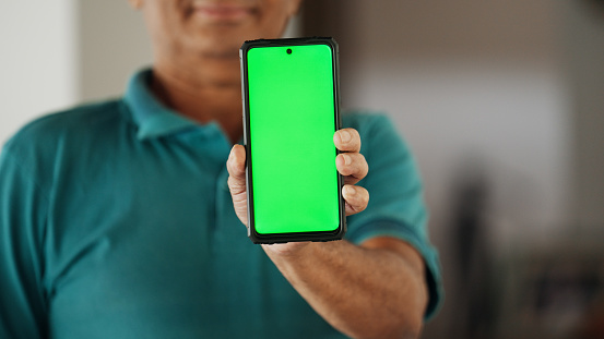 Close-up of a mature man smiling and holding up a smart phone with a blank green screen