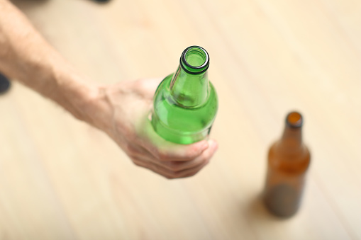 a person holds a green bottle in his hand against the background of wooden boards