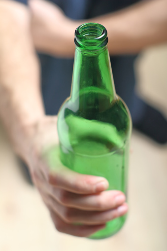 a person holds a green bottle in his hand against the background of wooden boards