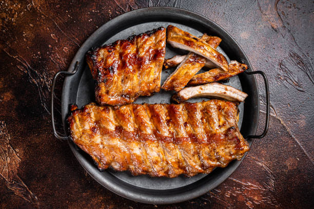 BBQ pork spare ribs St Louis with hot honey marinade in a steel tray. Dark background. Top view BBQ pork spare ribs St Louis with hot honey marinade in a steel tray. Dark background. Top view. plate rack stock pictures, royalty-free photos & images