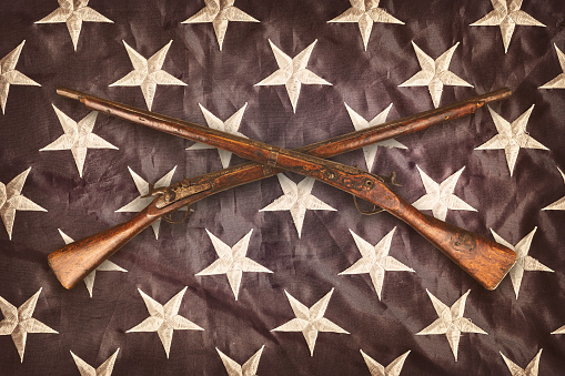 Two crossed vintage wooden rifles in front of the stars of the American flag