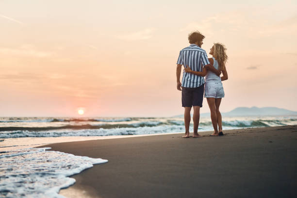 istock Back view of embraced couple talking on the beach at sunset. 1469169025