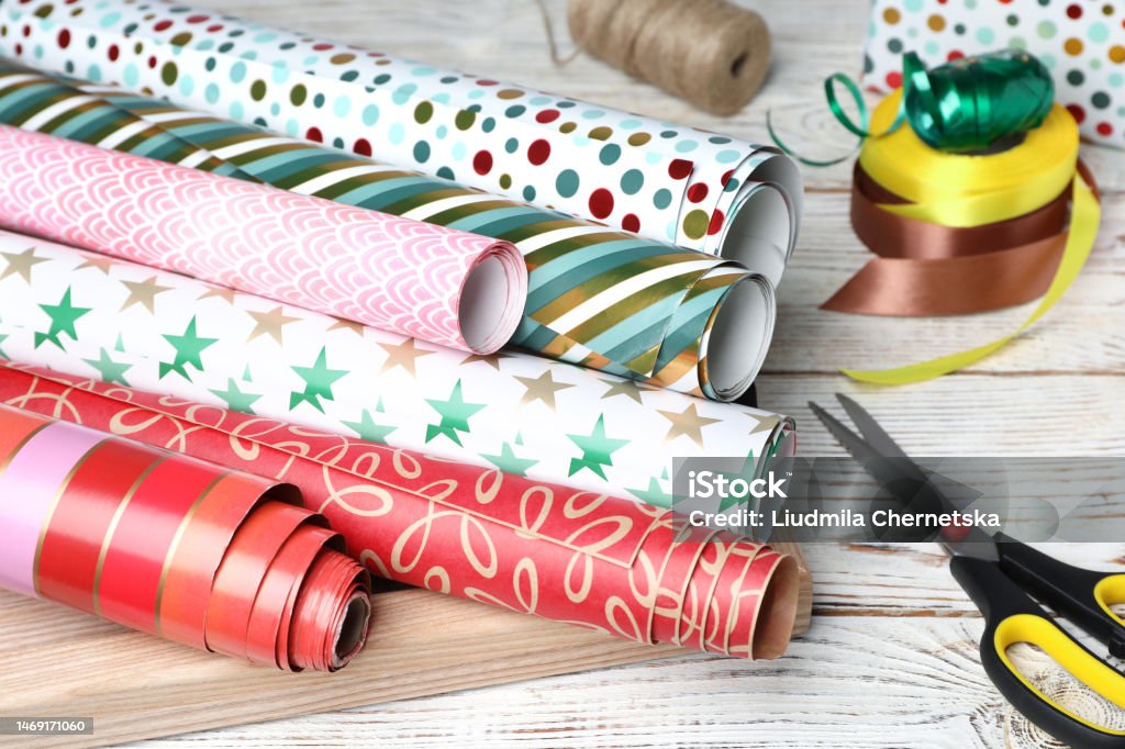 Different Colorful Wrapping Paper Rolls Scissors And Ribbons On White  Wooden Table Stock Photo - Download Image Now - iStock