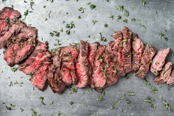 Grilled sliced Machete beef meat steak on steel tray with thyme. Black background. Top view Grilled sliced Machete beef meat steak on steel tray with thyme. Black background. Top view. flank steak stock pictures, royalty-free photos & images