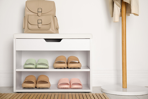 Storage cabinet with different pairs of rubber slippers near white wall in room